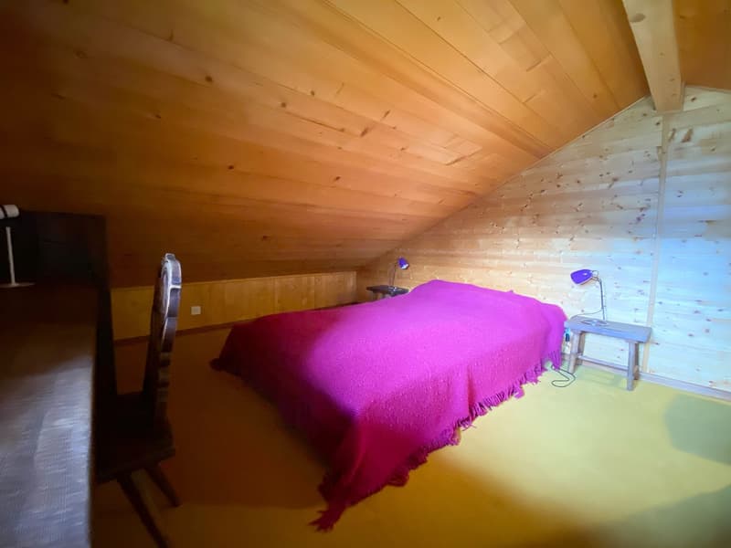Small bedroom with wooden bed, lamp, chair, wooden walls, and desk