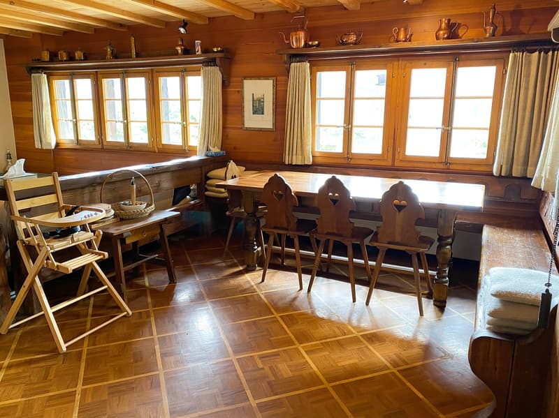 Dining room with wooden bench seating, wooden dining table and chairs, wooden parquet floor, large windows with curtains