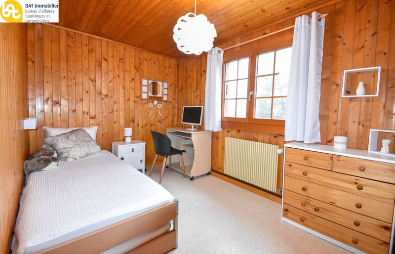 Cozy wooden bedroom with a single bed, dresser, desk, and large windows providing natural light