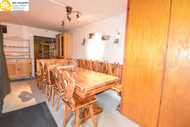Large wooden dining table with matching chairs, wooden cabinets and shelves, lighting fixture on the ceiling