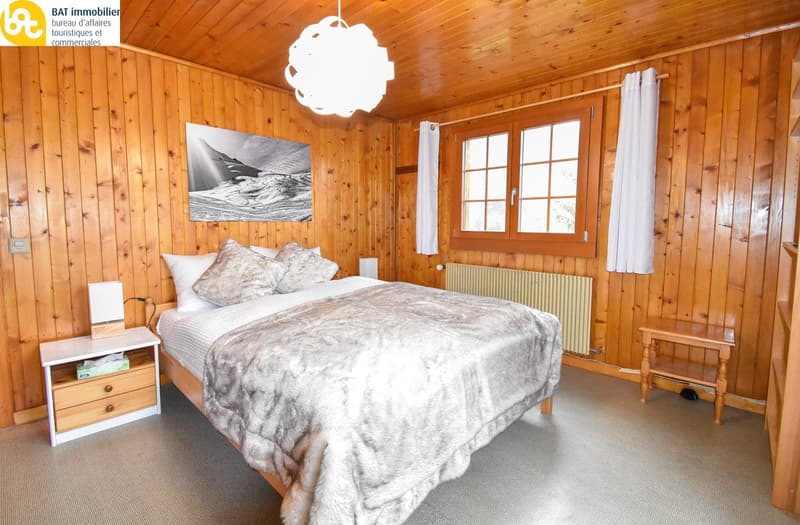 Cozy wooden bedroom with a large bed, wooden walls and ceiling, a hanging light fixture, and a framed artwork on the wall