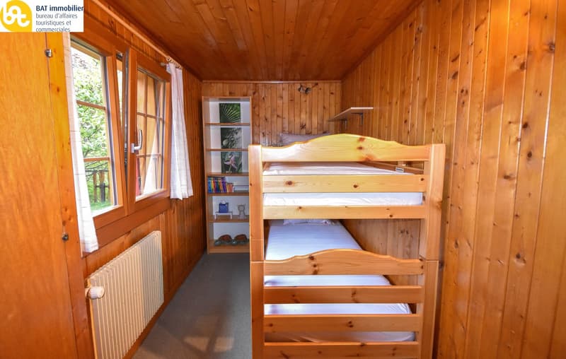 Wooden cabin-style bedroom with bunk beds, shelving unit, and large window overlooking a balcony or terrace