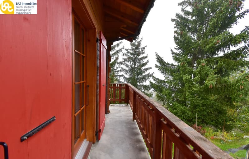 Wooden cabin with a covered balcony/terrace, surrounded by lush green trees
