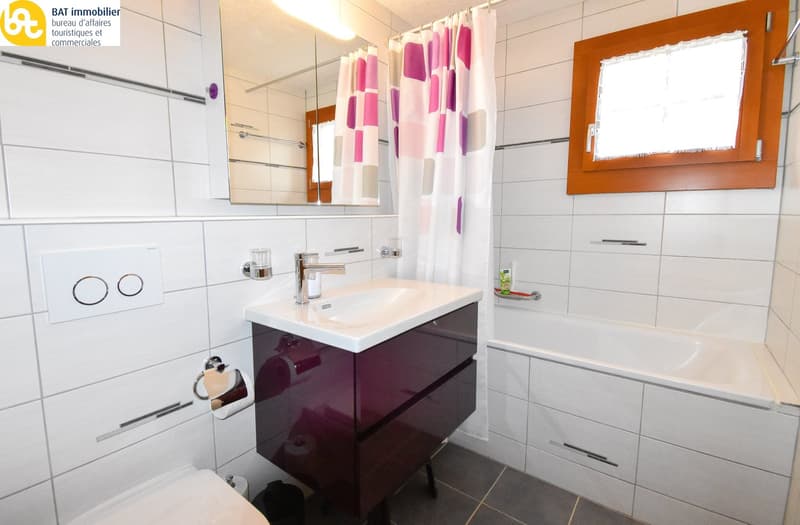 Spacious bathroom with white and purple tiled walls, a vanity unit with a sink, a shower curtain, and a mirror on the wall.