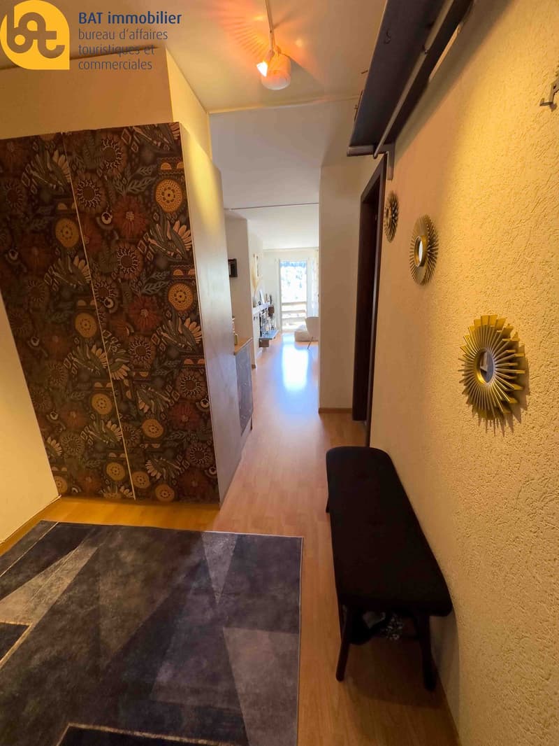 The image shows a hallway with a patterned wall panel, a tiled floor, and decorative wall accents. The hallway leads to another room, which can be seen in the background.
