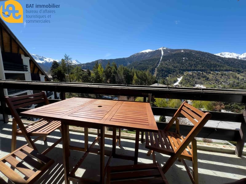 Wooden table and chairs on a balcony with a scenic view of snow-capped mountains and a ski slope in the distance
