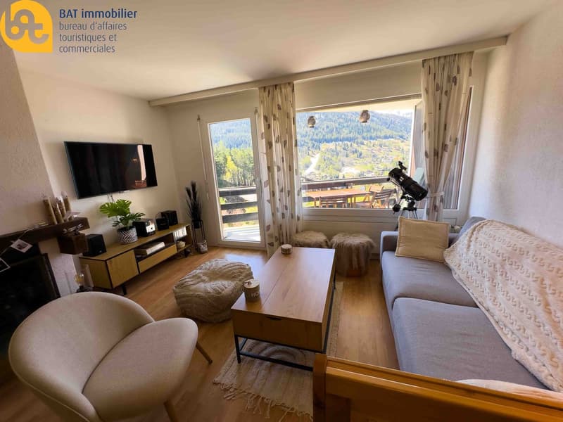 Spacious living room with large windows offering a scenic mountain view, hardwood floors, couch, coffee table, TV stand, and telescope for enjoying the natural surroundings.