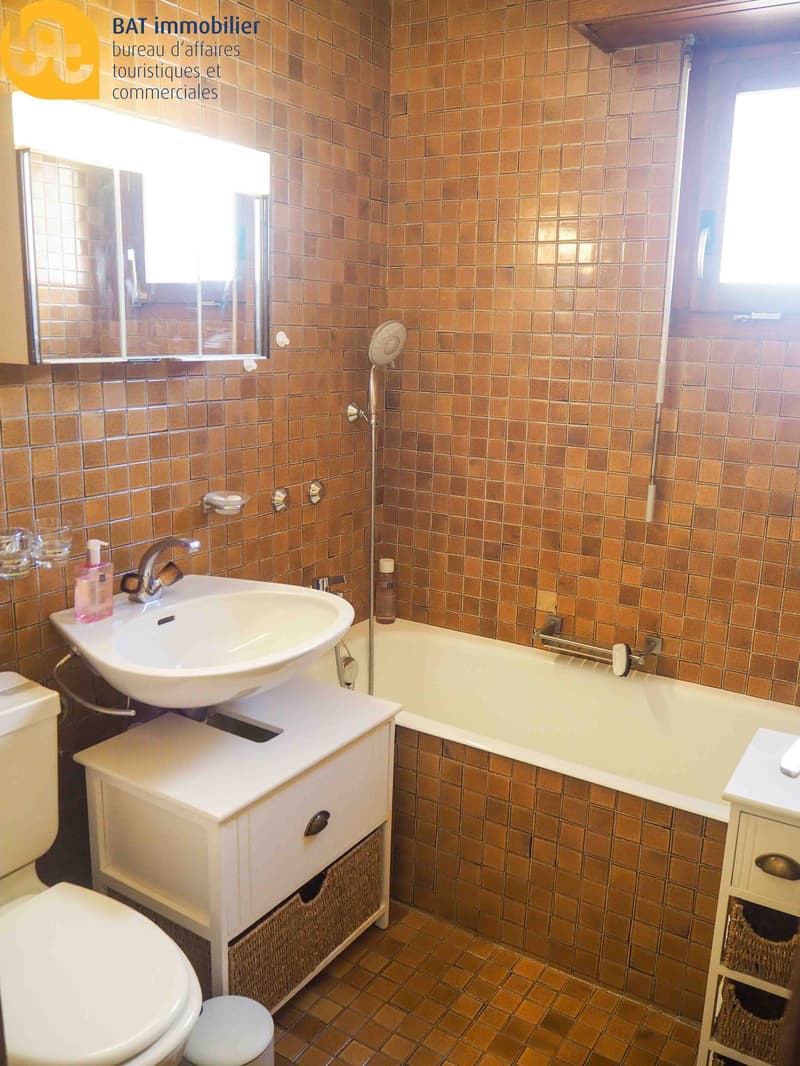 Tiled bathroom with a bathtub, sink, and storage cabinet. The walls are covered in orange/brown tiles and there is a private washing machine visible.