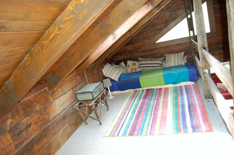 Wooden beams and paneling, colorful striped bedding, small table and chair, cozy and rustic atmosphere
