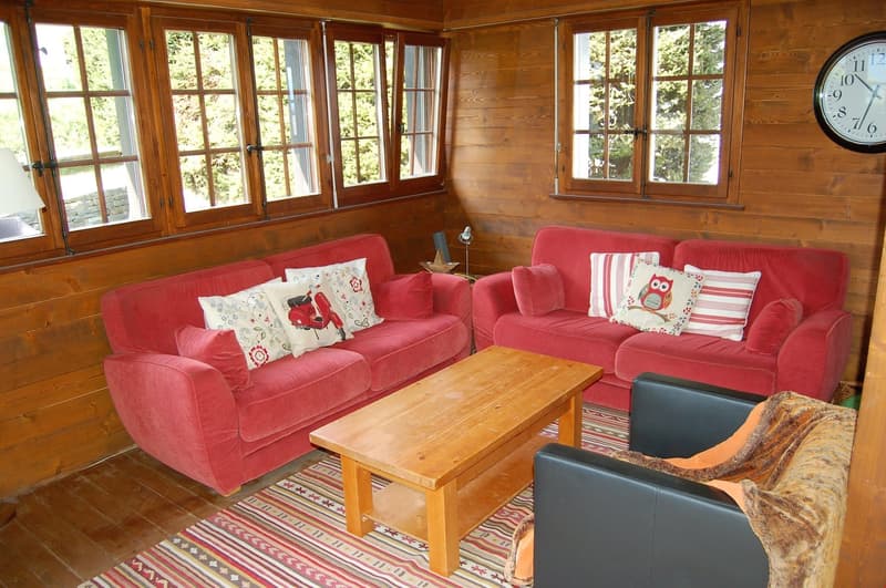 Cozy wooden cabin-style living room with large windows, red sofas, wooden coffee table, and a fireplace