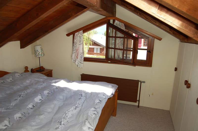 Cozy bedroom with wooden beams, large window, wooden furniture, and patterned bedding