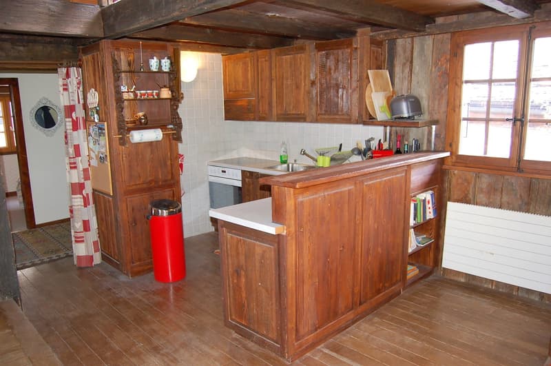 Rustic wooden kitchen with cabinets, shelves, appliances, and a tiled backsplash. The kitchen has a cozy, country-style feel with wooden beams and a window providing natural light.