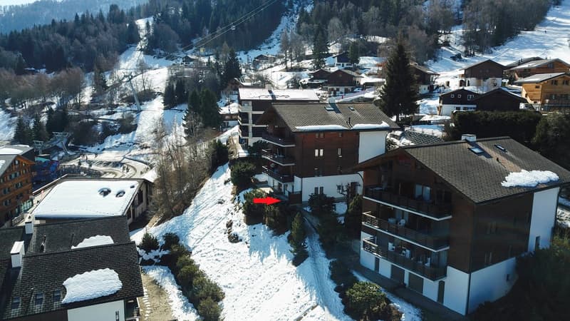 Aerial view of a snowy ski resort town with residential buildings, ski slopes, and ski lifts visible in the background.