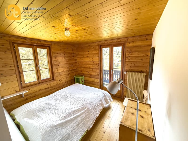 Cozy wooden bedroom with large windows, wooden ceiling, bed, and bedside table