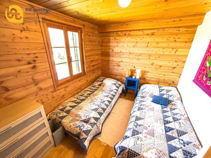 Wooden cabin interior with two single beds, patterned quilts, and a small side table