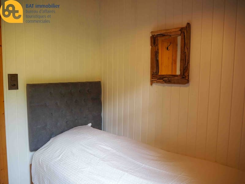 Bedroom with wooden paneled walls, a gray tufted headboard, and a rustic wooden framed mirror on the wall.