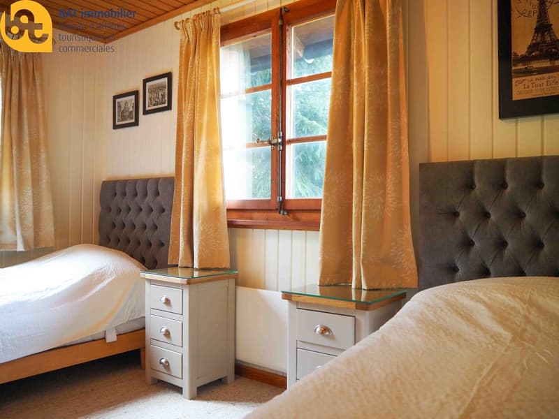 Cozy bedroom with wooden walls and large windows, tufted headboards, nightstands with drawers, and curtains covering the windows.