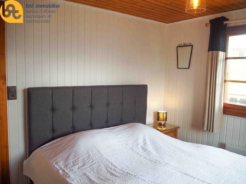Bedroom with wooden paneled walls, large headboard, bedside table with lamp, and curtains