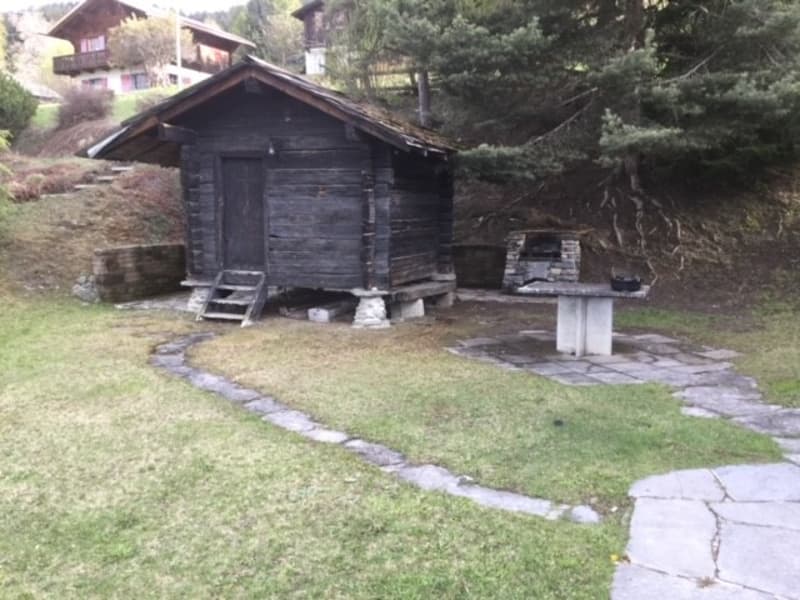 A rustic wooden cabin with a stone fireplace, surrounded by a grassy area and trees.
