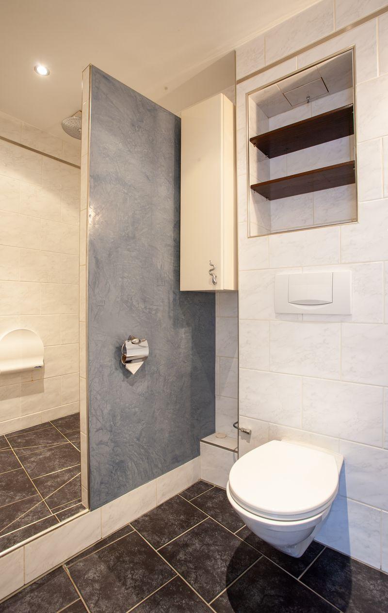 modern bathroom, white tiles, glass shower, storage cabinet, wall-mounted toilet, toilet paper holder
