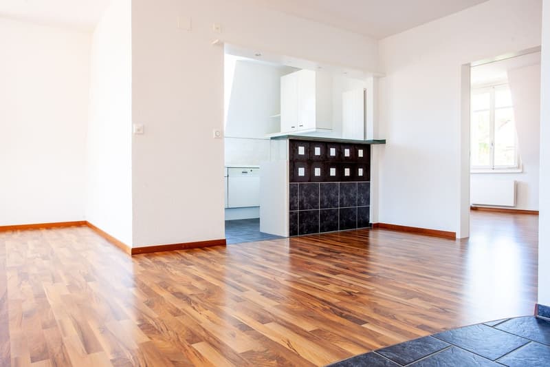 empty room, wooden floors, white walls, visible kitchen area