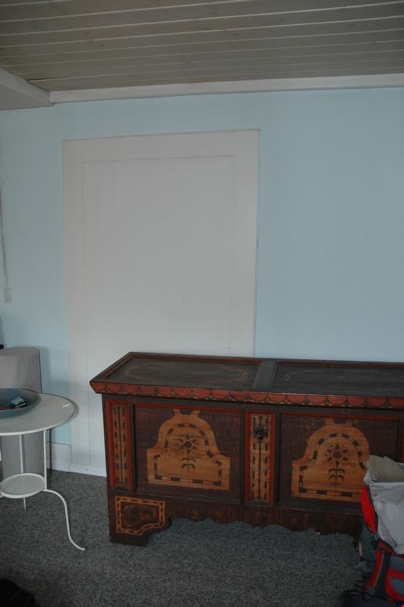 A room with a wooden chest, a white table, and a white door.