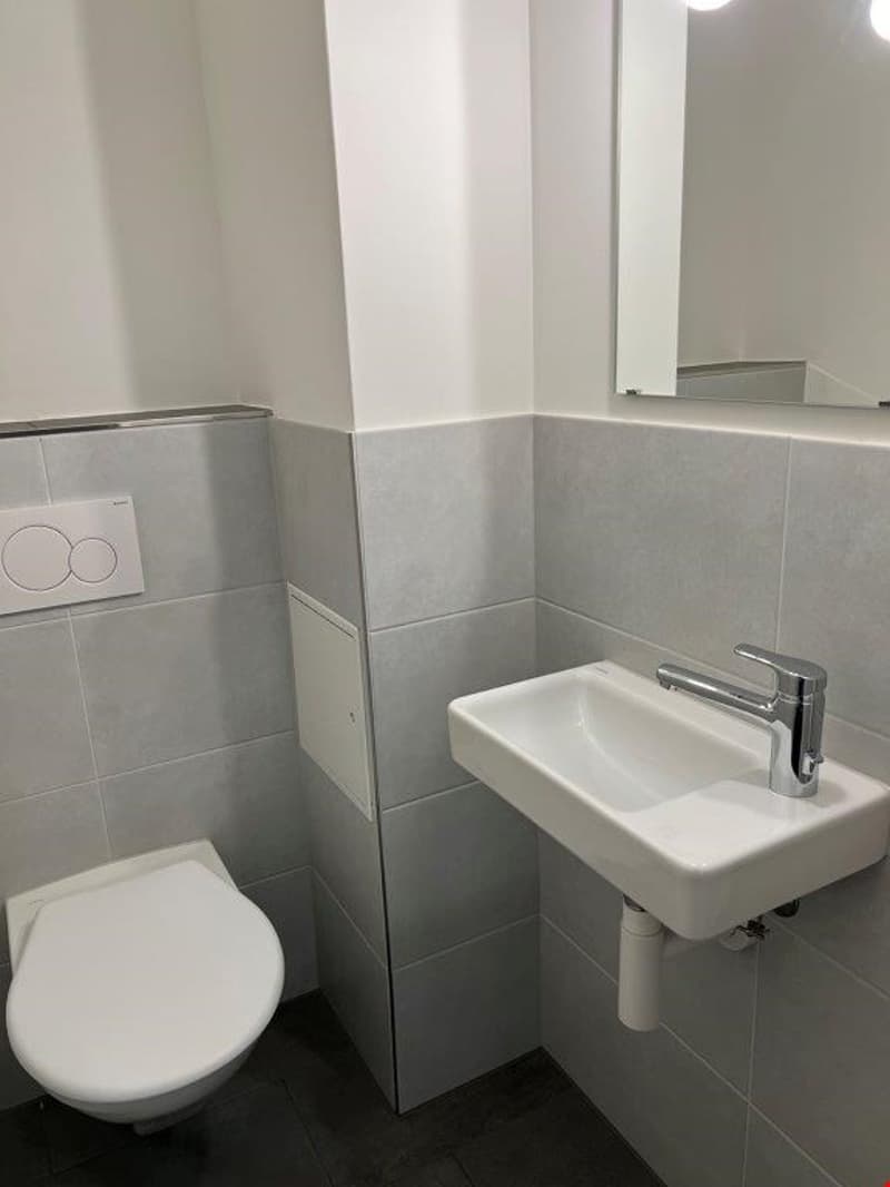 Compact bathroom with white toilet, sink, and tiled walls and floor