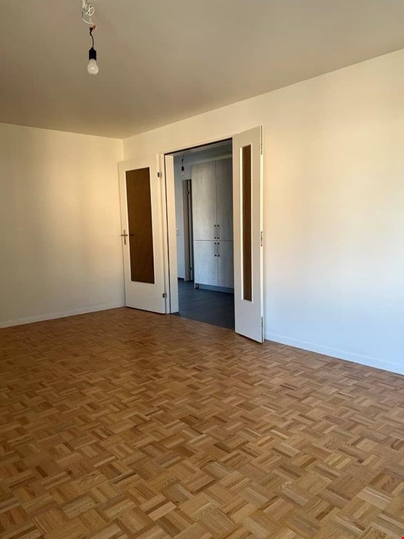 Empty room with hardwood parquet flooring, white walls, and two doorways leading to other rooms.