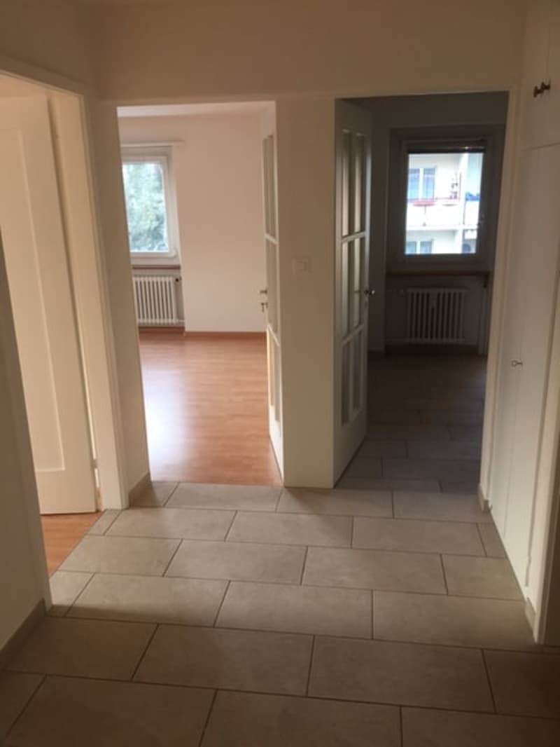 Empty room with wooden floor, white walls, two doors, and windows