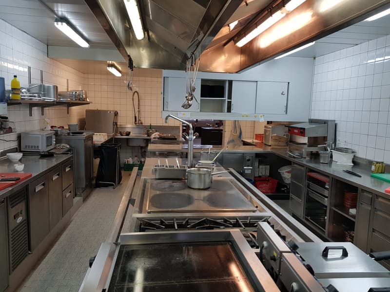 fully equipped kitchen, with stoves, baking ovens, sinks, kitchen appliances and utensils, tiled walls, stainless steel appliances, various cooking utensils and containers, shelves, exhaust hood