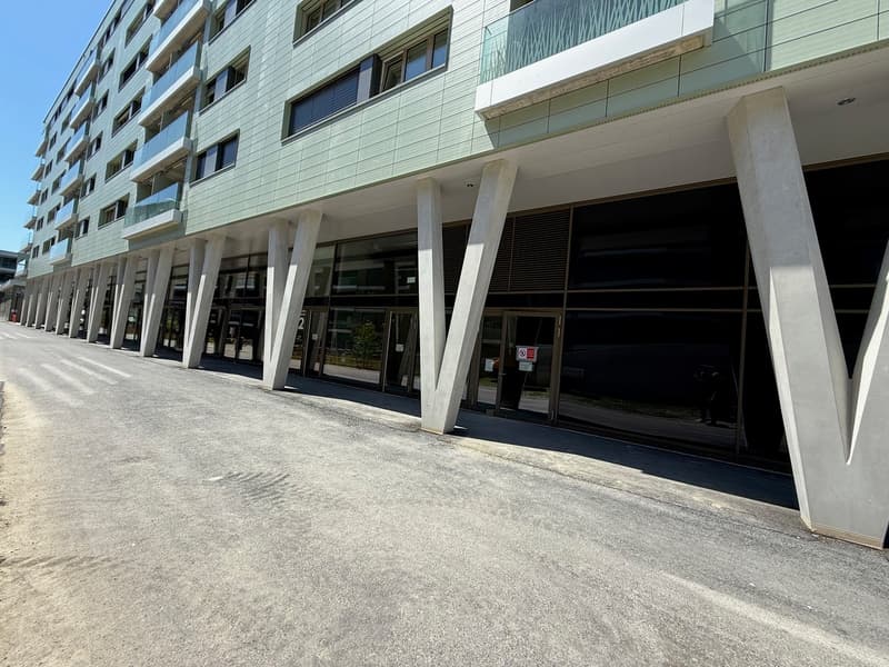 Multi-story commercial building with glass windows and doors, concrete columns, and a parking area in front.