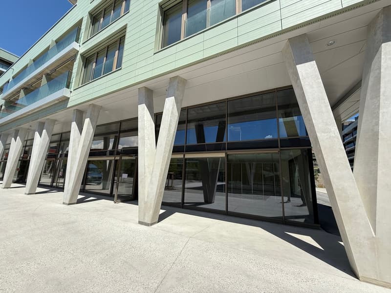 A modern multi-story commercial building with a glass facade, concrete columns, and a raised entrance area.