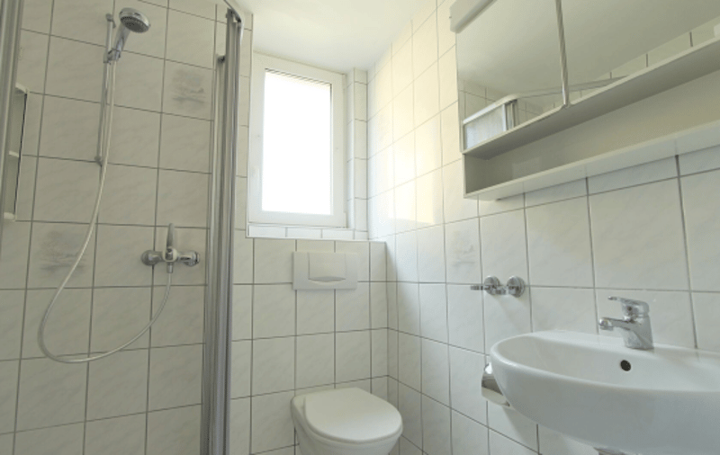 Bathroom with white tiled walls, white sink, white shower, toilet, mirror, and cabinet