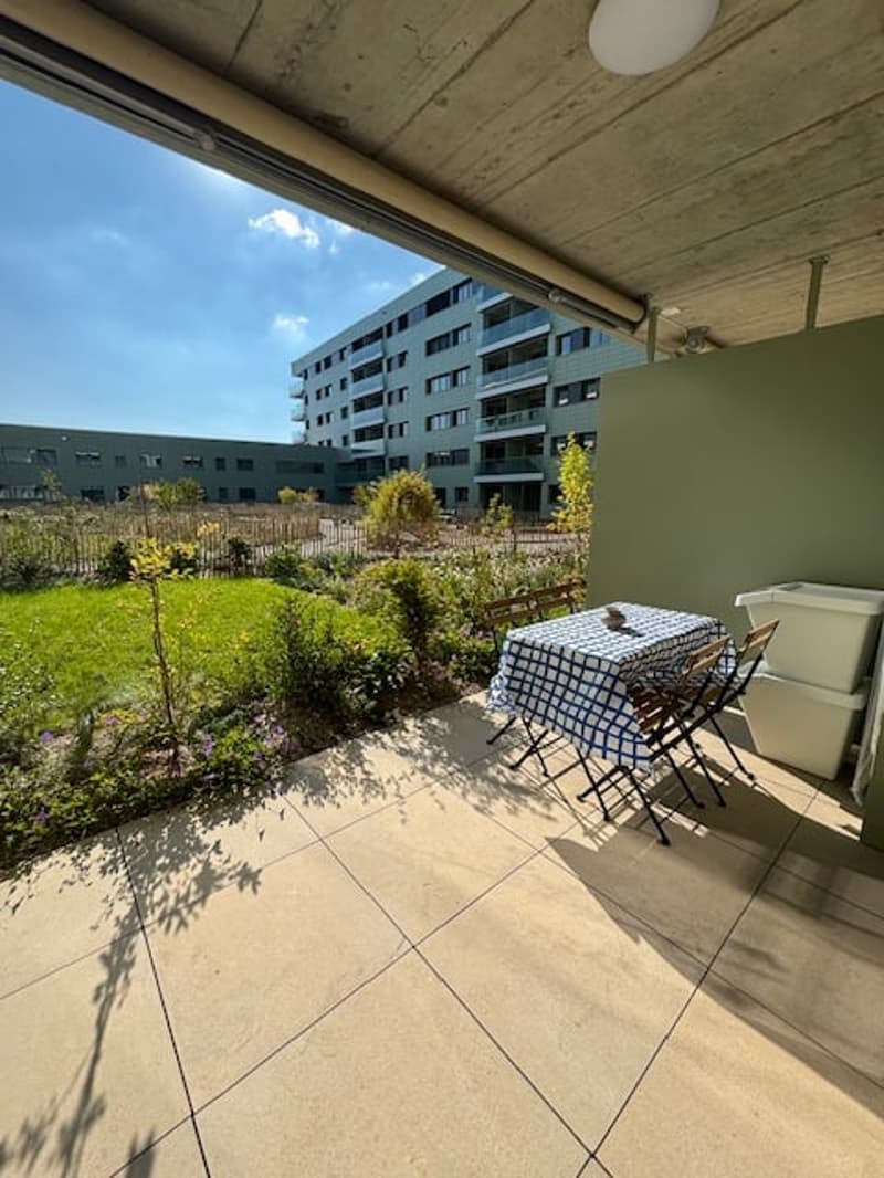 Tiled balcony area with garden view, table with 4 chairs, small flowerbeds