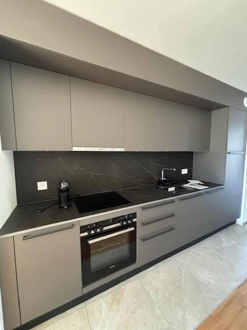 Kitchen with modern appliances and cabinets, black countertops, gray cabinetry, a stove and oven combo, a sink, and tiled flooring.