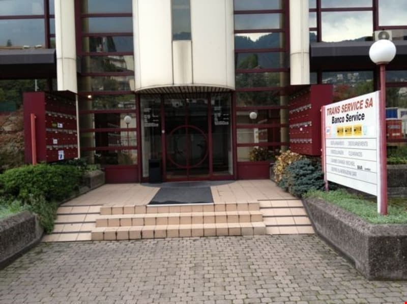 A commercial building with a glass entrance, brick and stone exterior, and a parking area in front.