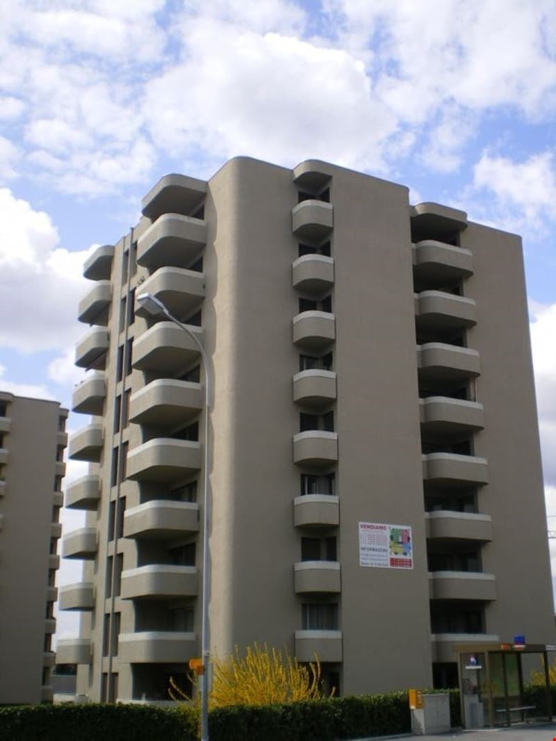 Multi-story apartment building with concrete exterior and balconies on each floor. The building has a modern, geometric design with stacked rectangular units.
