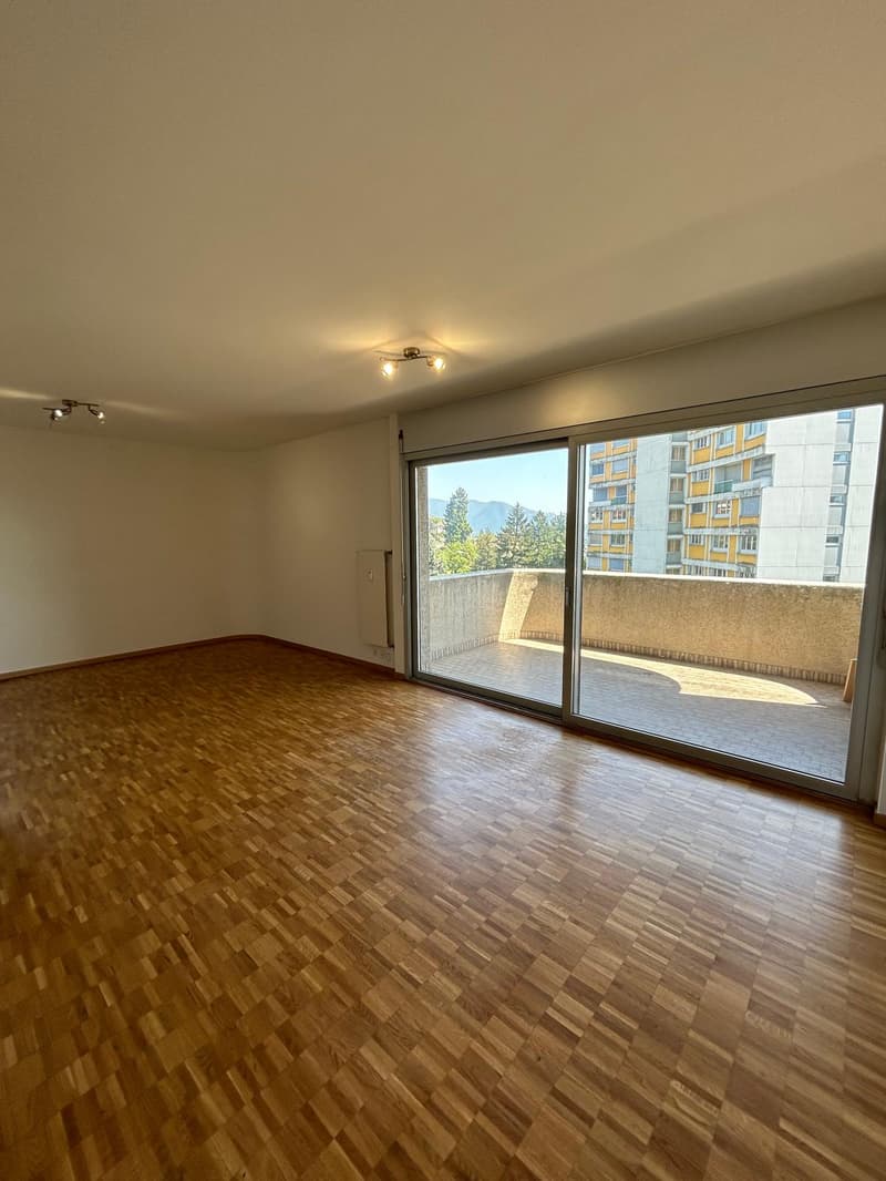 Spacious living room with hardwood flooring, large windows providing natural light, and access to a balcony or terrace.