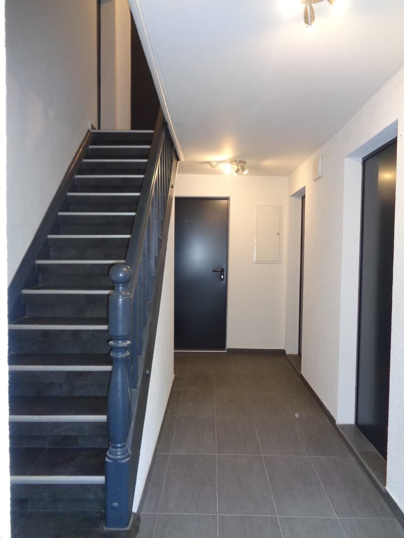Tiled hallway, closed door, grey tiled floor, staircase, lights on the ceiling