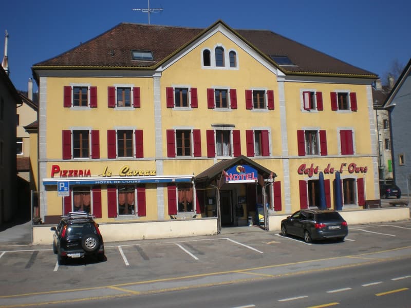 2 story building, yellow exterior, red shutters, brown roof, 2 cars parked in front, sign for hotel and pizzeria