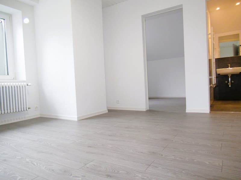 empty room, white walls, wooden floor, window, radiator, door to bathroom