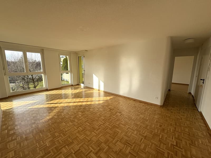 empty room with wooden parquet flooring, white walls, windows with balcony, hallway leading to other rooms
