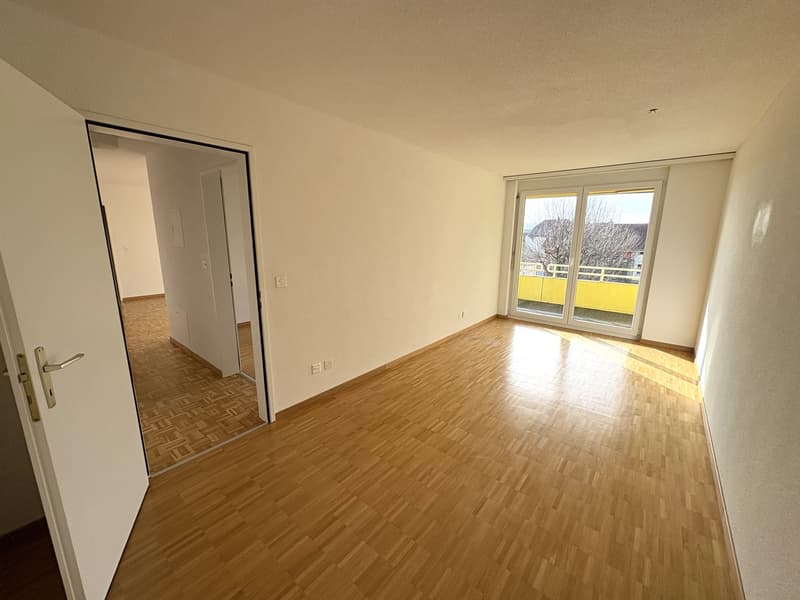 Empty room with wooden floors, glass sliding doors leading to balcony, white walls and ceiling