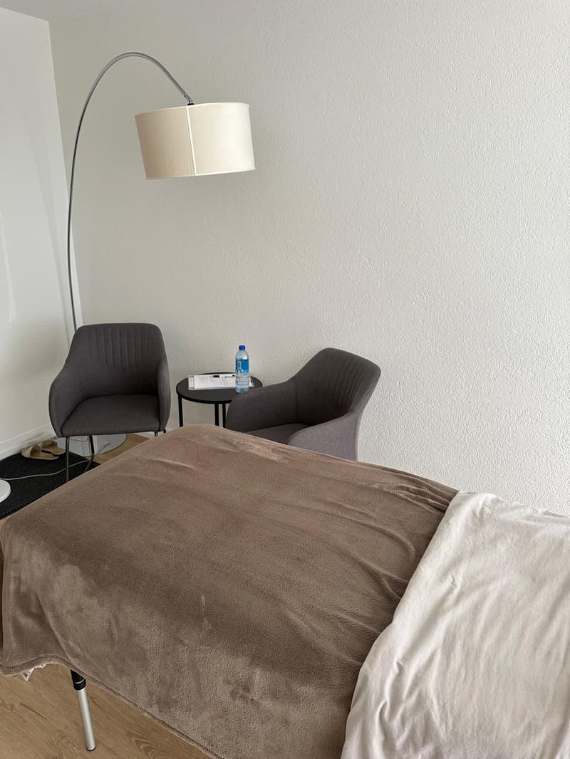 a bed, 2 grey chairs, black coffee table, lamp, black rug