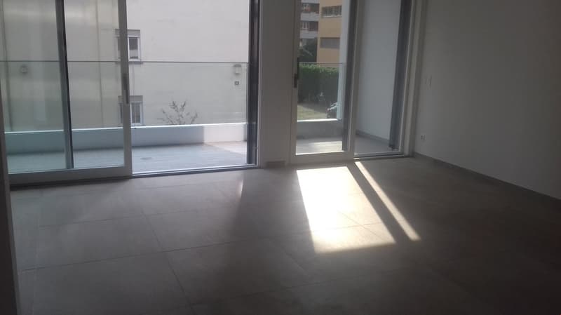 Large open space with floor-to-ceiling windows, grey tile flooring, and a balcony or terrace visible through the glass doors.