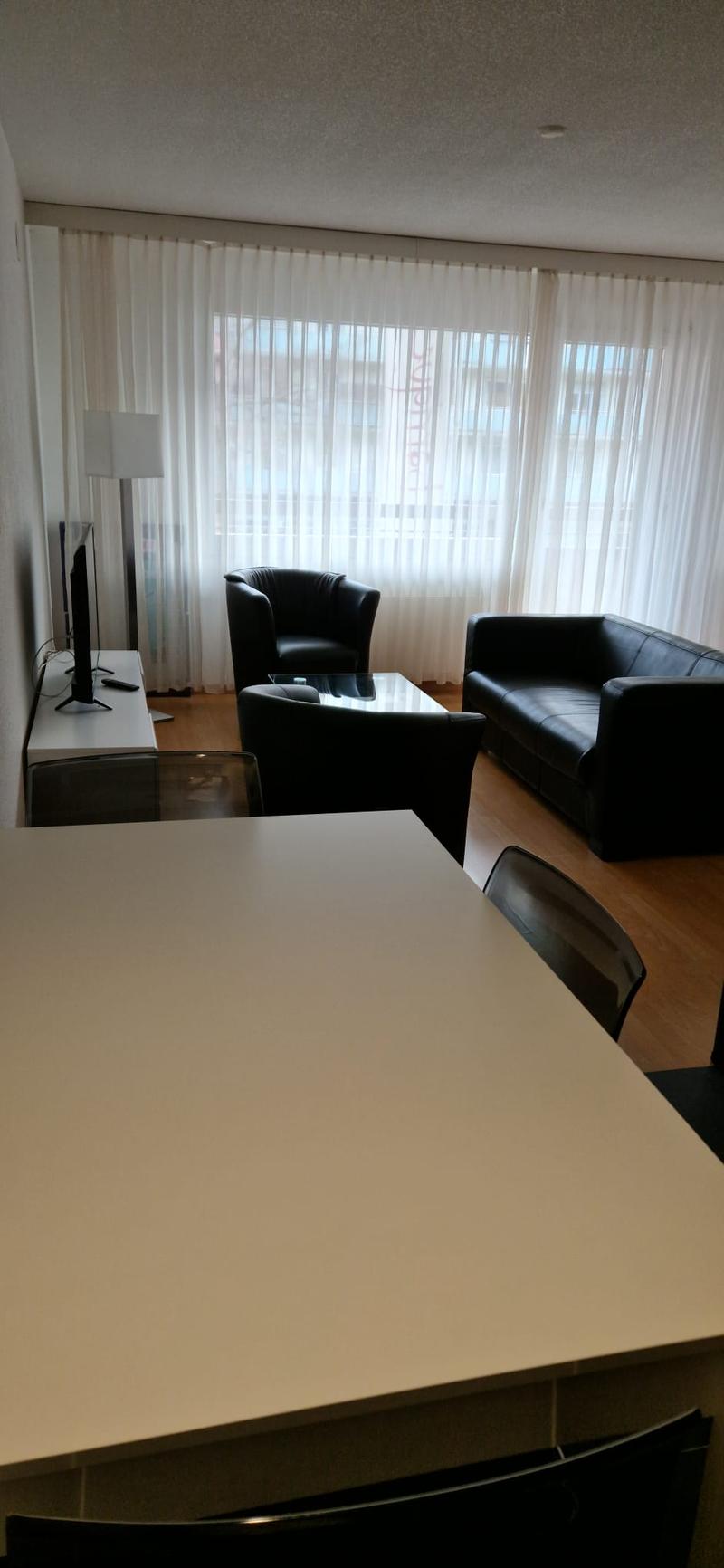 black leather couch, white walls, hardwood floor, large windows, large screen tv, glass coffee table, table and chairs, lamp