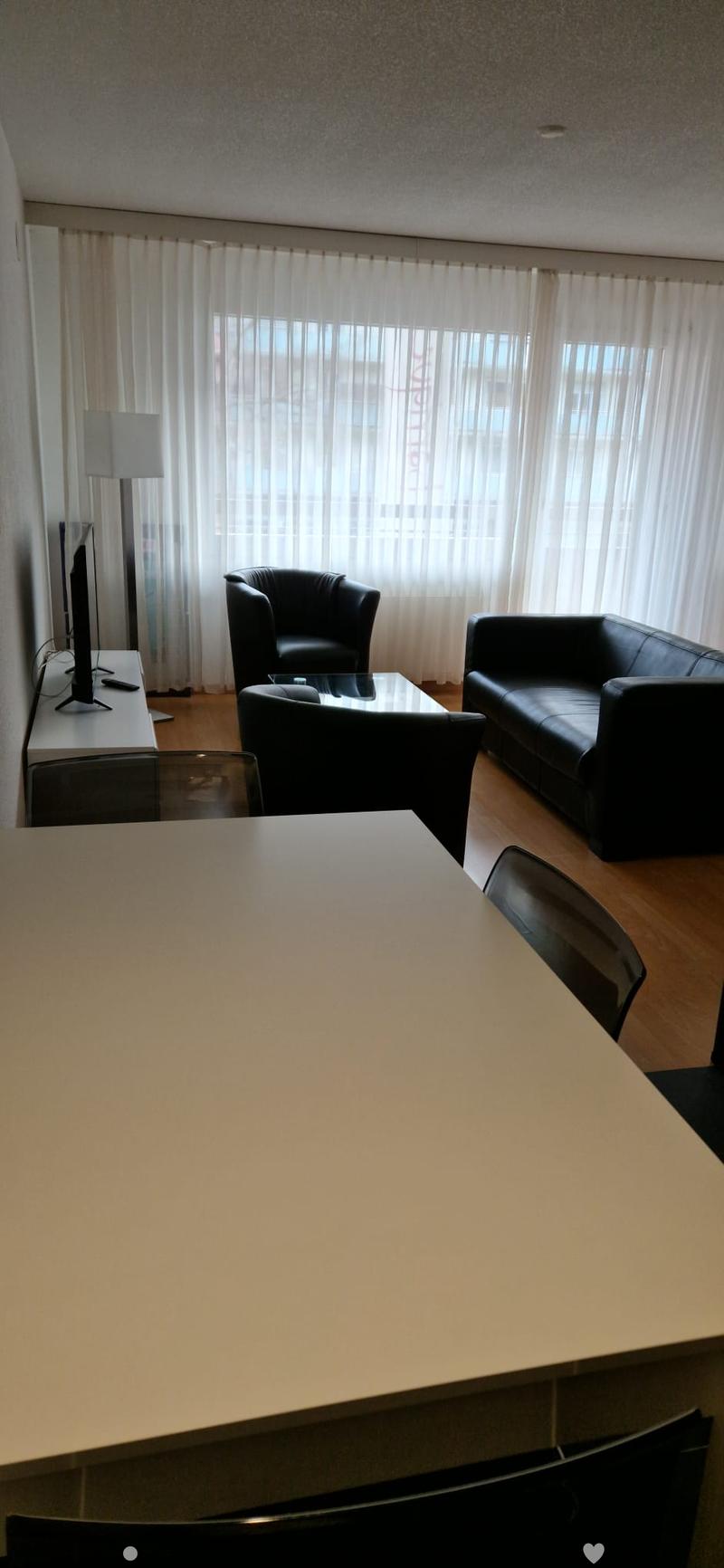 black leather couch, white walls, hardwood floor, large windows, large screen tv, glass coffee table, table and chairs, lamp