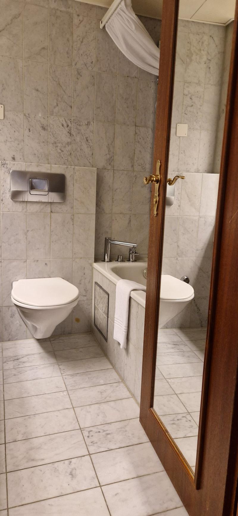 Bathroom with a toilet, bathtub, and shower area, all marble tiled, modern fixtures