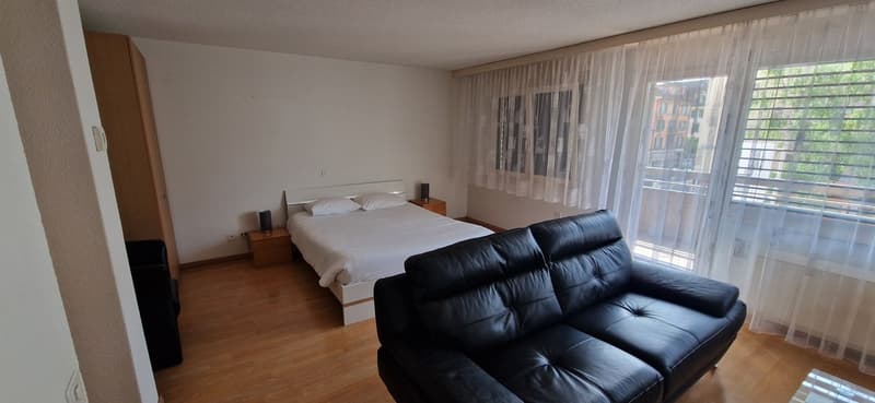 Room with a bed, sofa, two nightstands, wooden floor, a small balcony and windows with curtains.