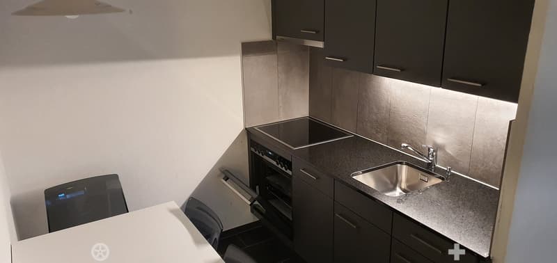 Modern kitchen with tiled walls, granite countertops, stainless steel sink, dishwasher, integrated oven, and a set of dark cabinets.